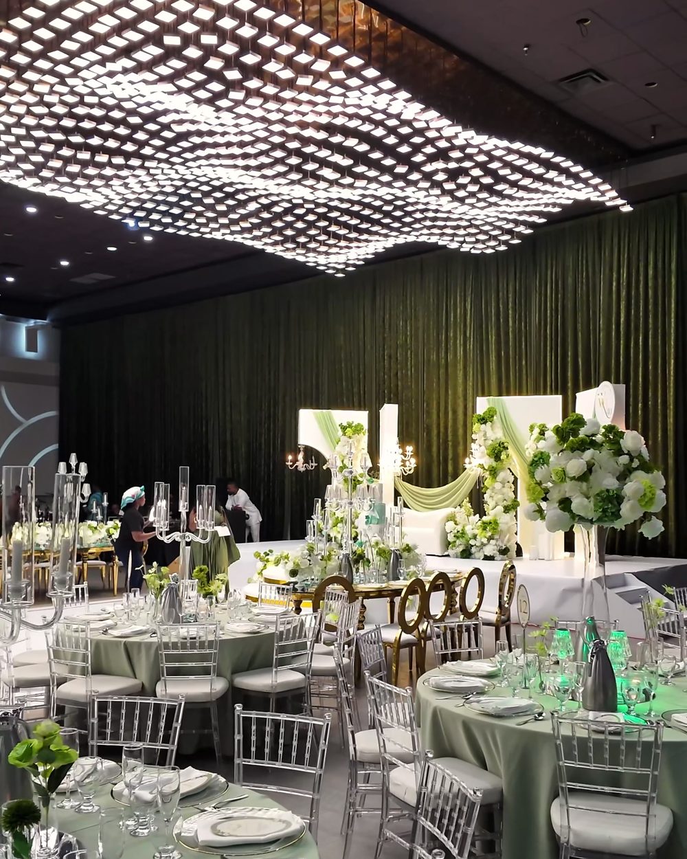 Ballroom with a sculptural crystal chandelier over sage-dressed round tables
