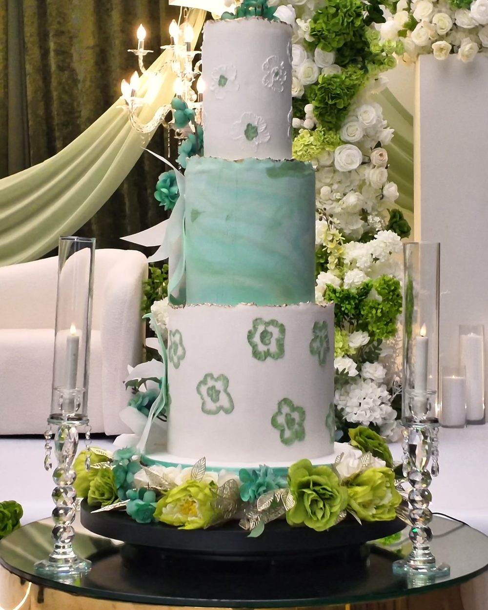 Mint and white tiered cake surrounded by white roses and crystal candle holders