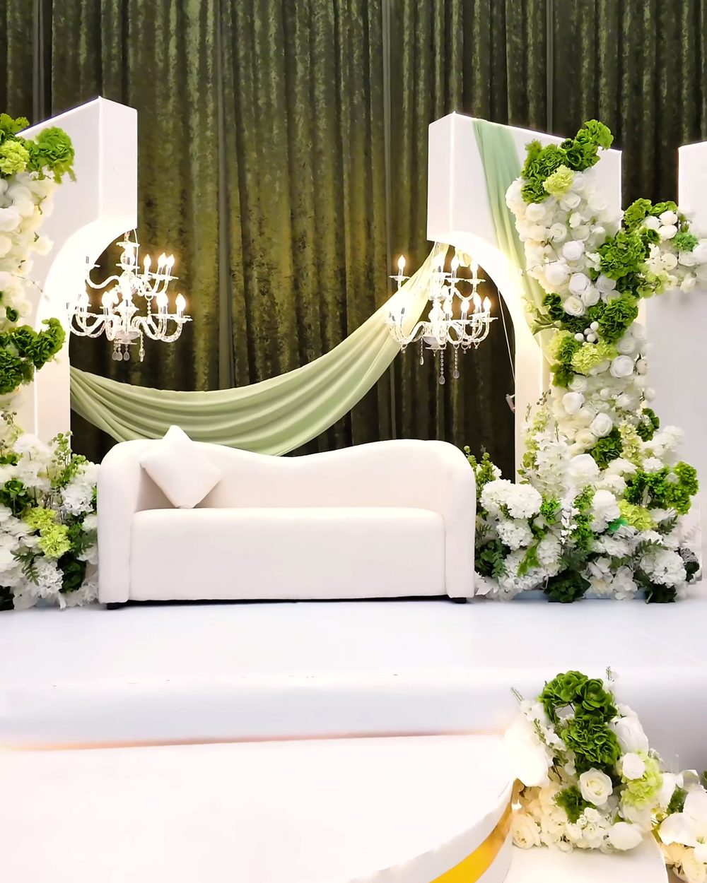 Celebration stage with a white sofa, sage drapery, chandeliers and gold-trimmed steps